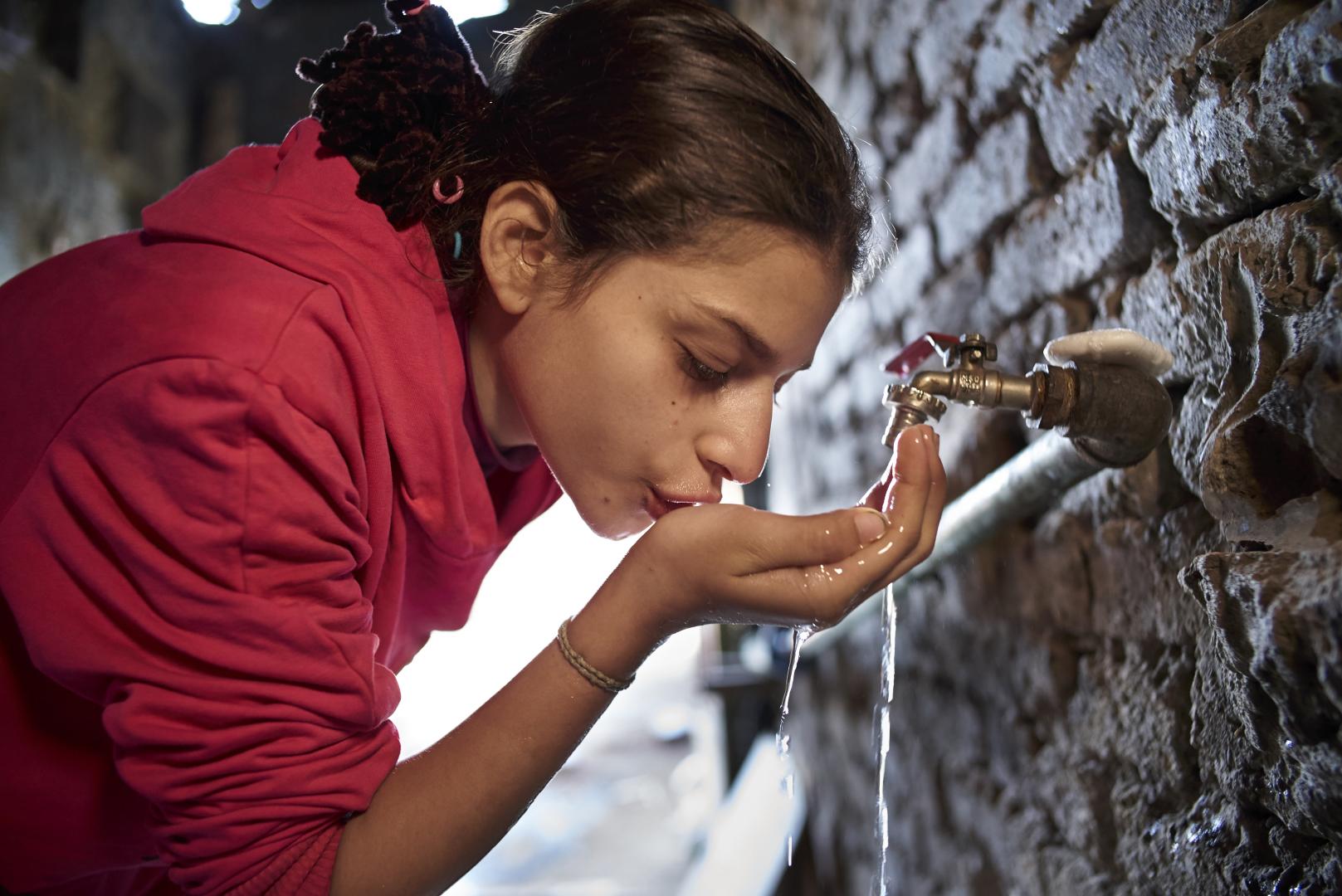 Aya, 12 years old, drinks water from a tap in her house in a slum in Ezbet Khairalla neighbourhood. 